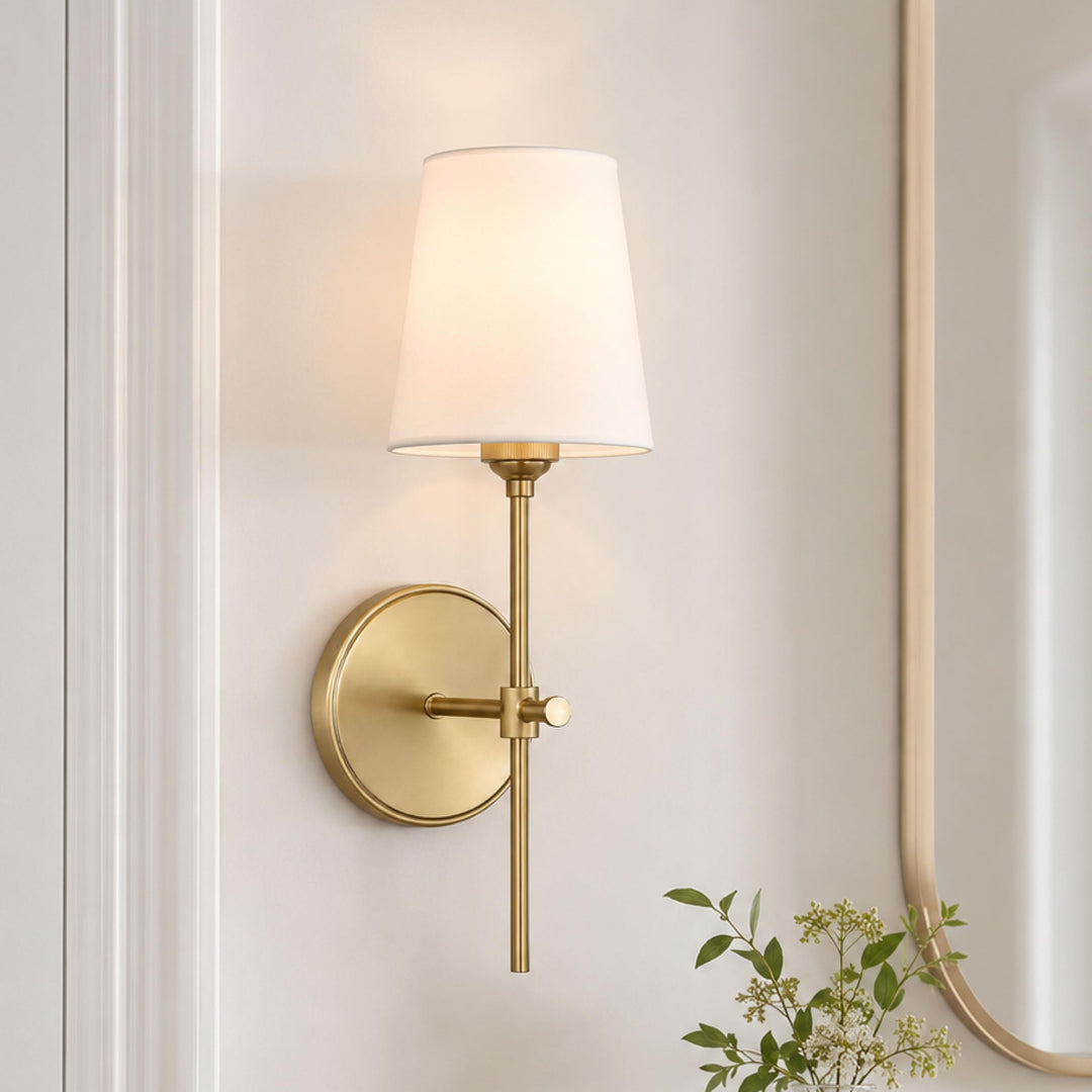 Satin brass Baker sconce lit on a wall beside an arched mirror