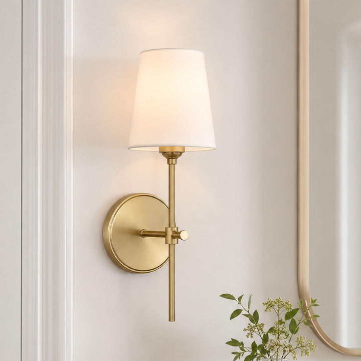 Satin brass Baker sconce lit on a wall beside an arched mirror