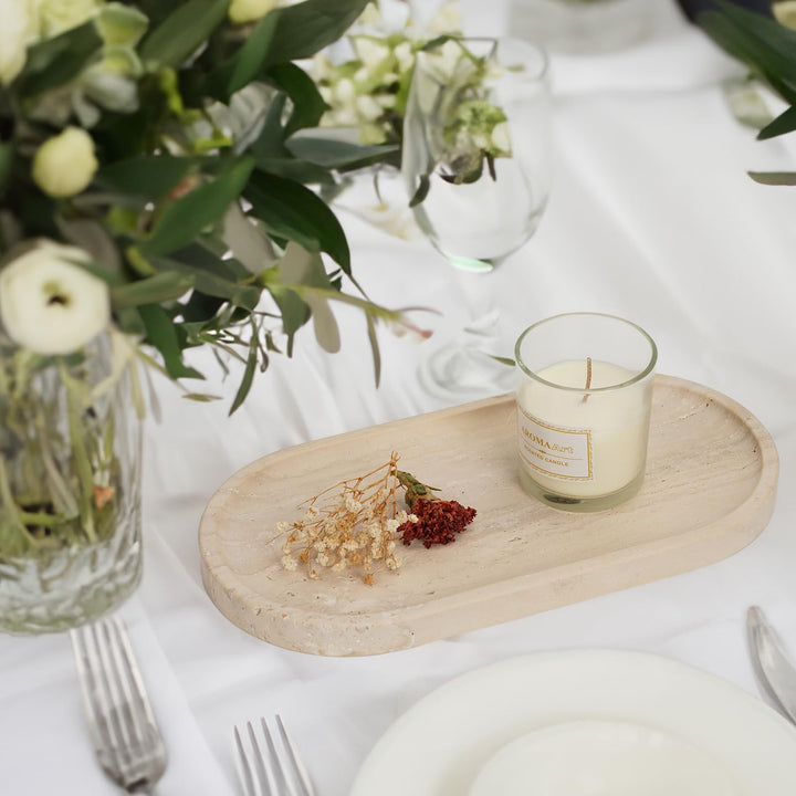 Travertine tray with a candle and dried flowers as a table centerpiece among plates, glasses and greenery