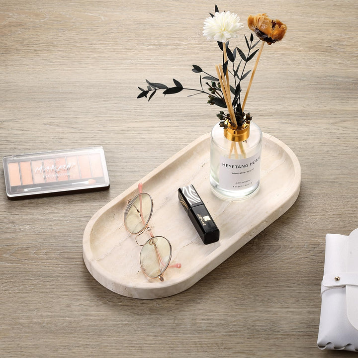 Travertine tray on a wooden desk holding glasses, a lipstick and a small vase of dried flowers